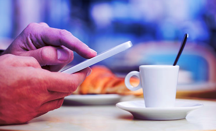Business owner applying for a business loan through their phone with a coffee next to them.