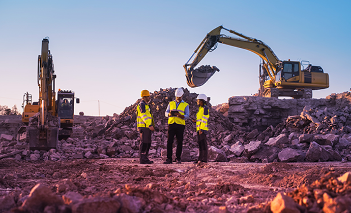 Three people in hi-vis vests stand in a land moving area with two yellow good assets on either side.