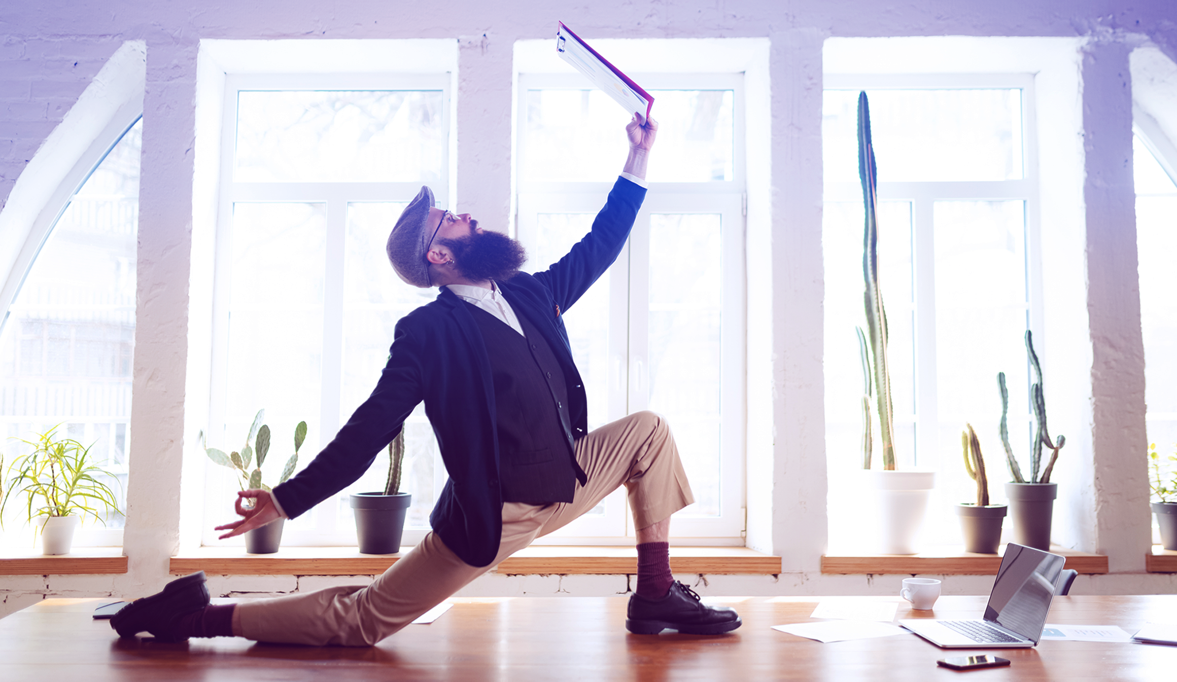Business professional striking a dynamic pose on a desk with a laptop and documents, symbolising balance and a healthy business mindset.